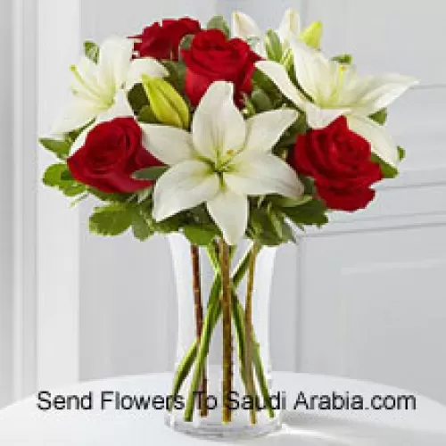 Rosas rojas y lirios blancos con algunos rellenos estacionales en un jarrón de cristal
